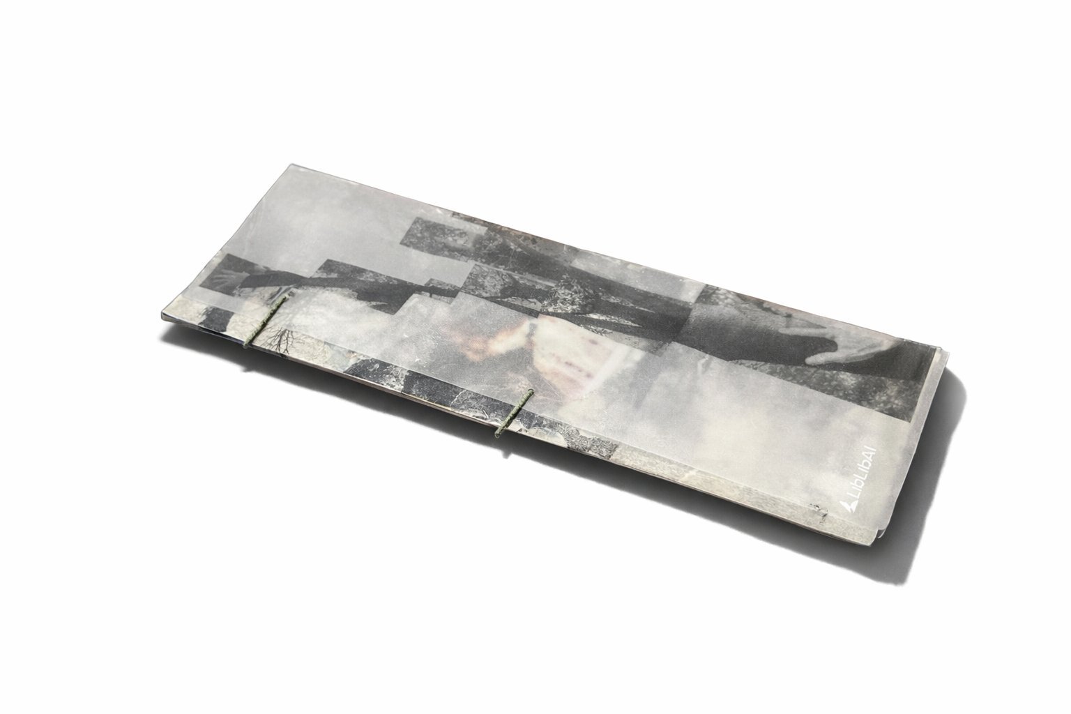 The zine at rest on a white field — closed, tracing-paper wrapped, threads visible at the spine.