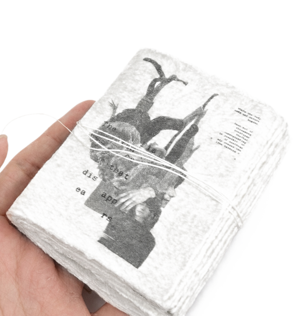 The zine, held in the hand, wound with thread — bark and figure visible across the front.